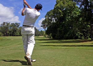 Man dressed in white clothes playing golf on sunny day