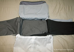 Second pair of trousers layed over two shirts as fourth stage of bundle warpping packing