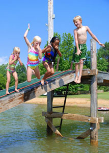 Four children jumping off a small bridge into a water