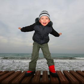 Young child making flying gesture on a seafront pier